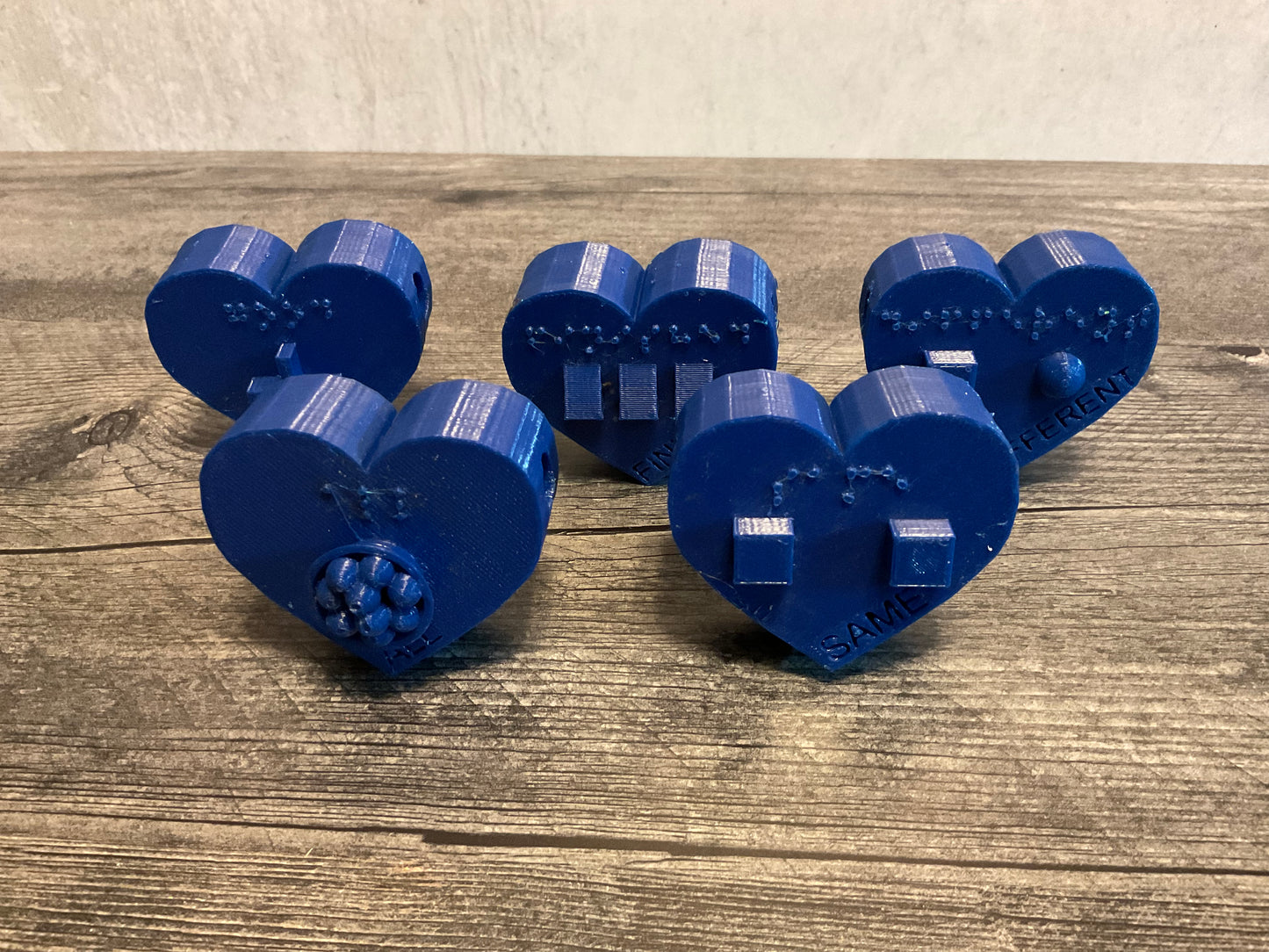 five blue heart shaped beads. Each has it's own symbol and braille as well as print Good Same Finished All Different