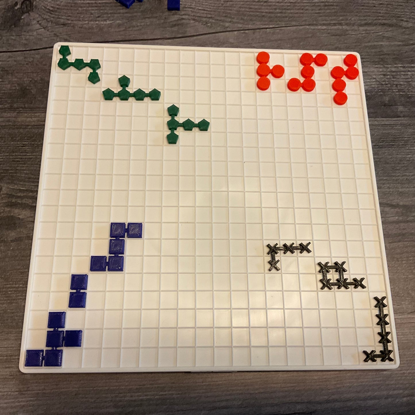 The Blockus board with the 3d printed tiles laid out on it. Each color has a different shape for tactile discrimination. The pieces are linked together into different shapes.