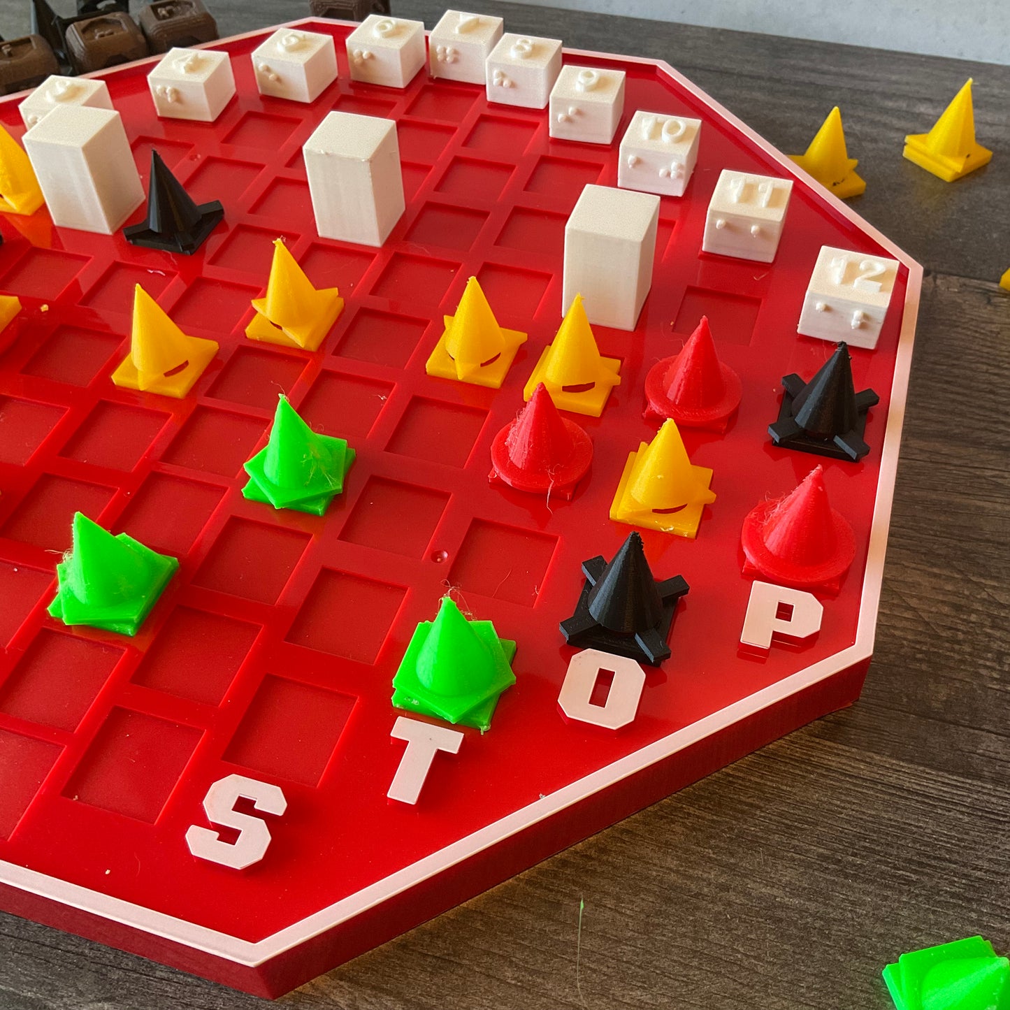 A picture of the other side of the board showing the pawns of different colors. Red has circles, yellow has triangles, black has xs and green has pentagons.