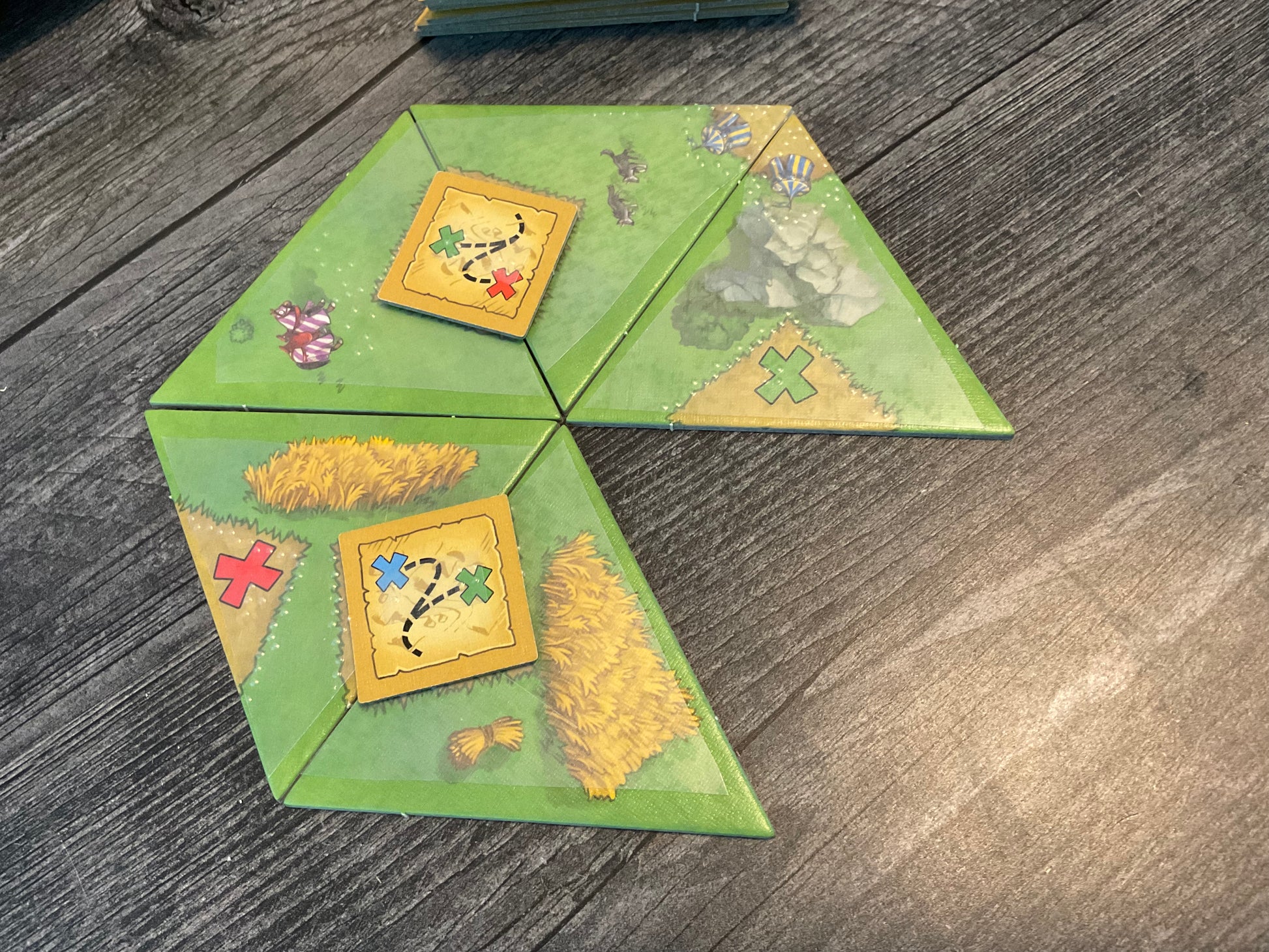 A close up of a partially built town. 2 completed task cards are on the board. Players can read the word horse in braille next to Conrad the Confused's horse. A partially built tournament is in the corner of the tiles.
