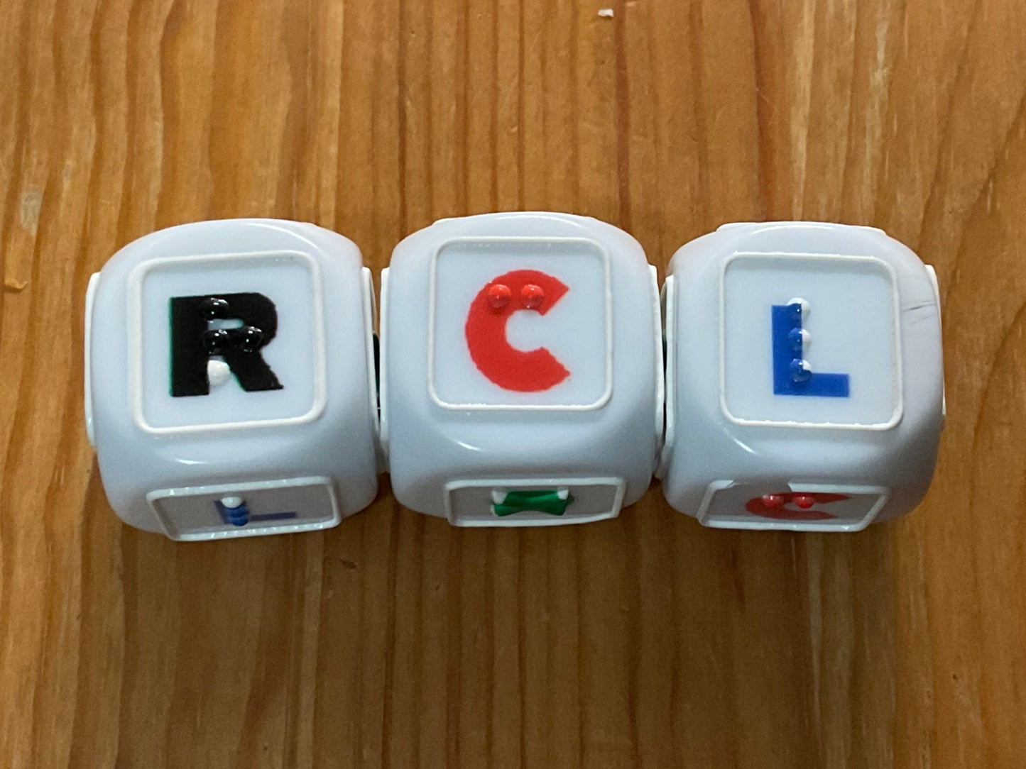 Close up on the LCR dice. Braille letter R is on r, Braille letter c is on c and surprisingly the braille letter L is on L. Not shown are the dots which have a tactile X on them(not the braille letter, just an X)