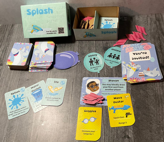The splash box with all the components laid out. The role cards are shaped like balloons, the attendee cards are shaped like party invitations, there are laser cut towel tokens and of course the actual cards.
