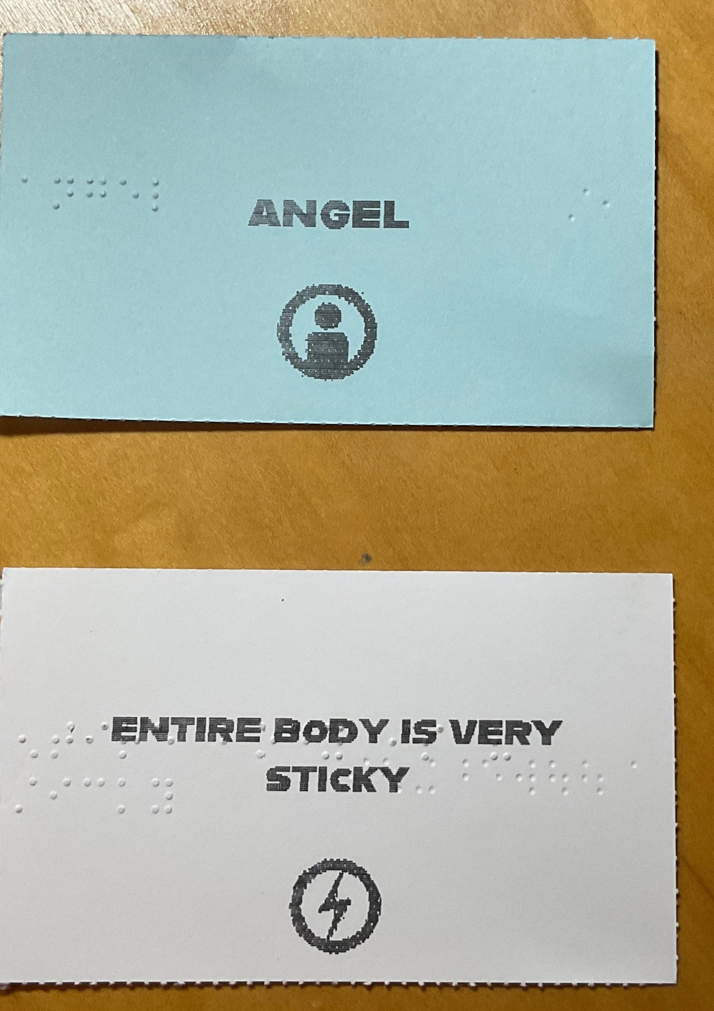 An example character card(angel) and example attribute card (entire body is very sticky) Both cards have large print and Braille on them