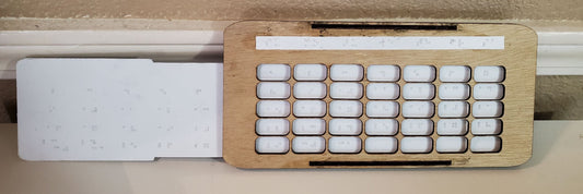 A white thermoformed sheet slides within a wooden base. The wooden base is 7 days across. The thermoformed sheet can be felt through the holes so that the correct dates are shown on the calendar.