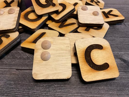 A pile of the braille letters. B showing the braille knobs and C showing the print are shown prominently in the front.