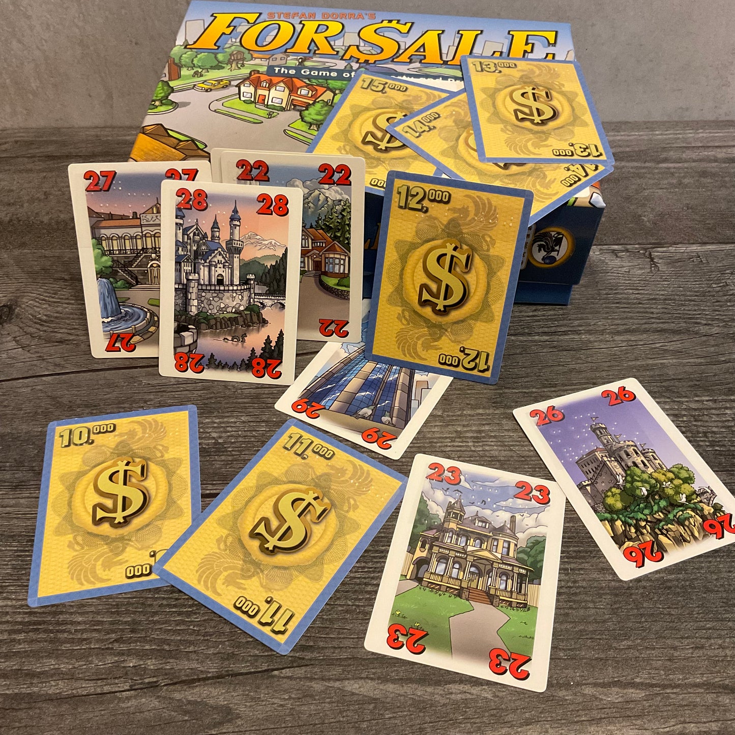 For Sale box with face up cards with houses and numbers on them as well as cards with money showing. All cards have braille stickers on them.