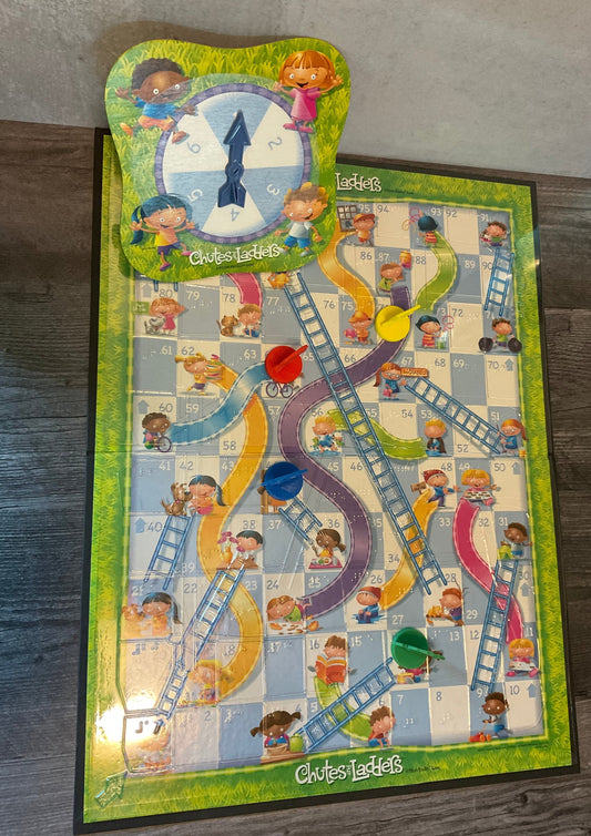 The chutes and ladders board. The spinner can be seen at the top with braille on it, a thermoformed clear board overlay with tactile ladders and chutes. The 3d printed pieces are also seen