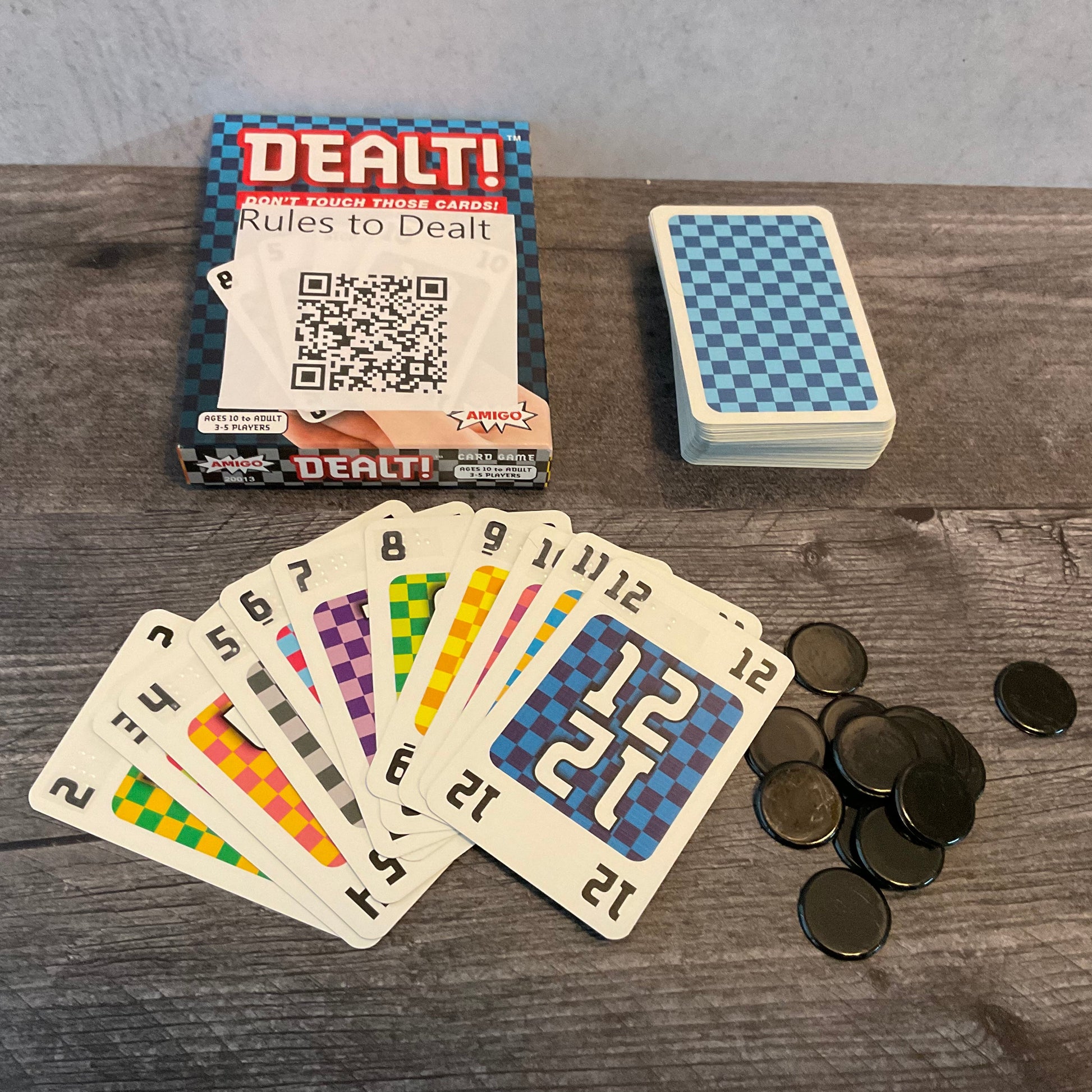 Dealt box with cards face up. The cards have transparent braille stickers on all of them from the accessibility kit. Black chips from the game are in the corner.