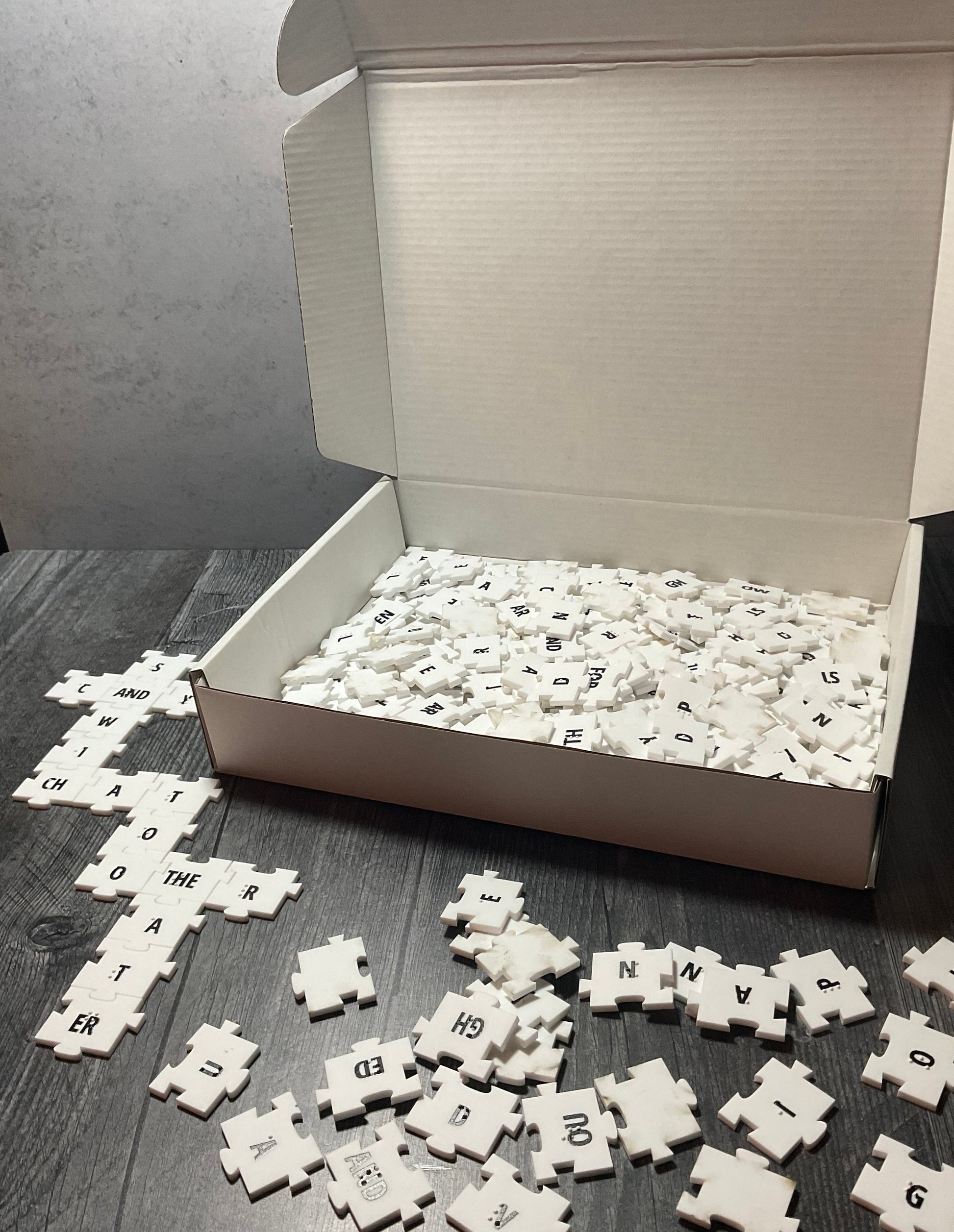 A picture showing the open box with a collection of tiles in front of it. Some of the tiles are forming a crossword grid.