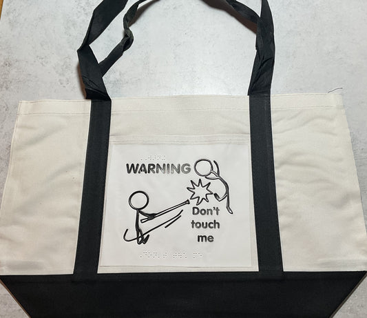 Tote bag with a picture of a blind stick figure whacking a person with a cane. The words "WARNING! Don't touch me!" are in both print and braille.