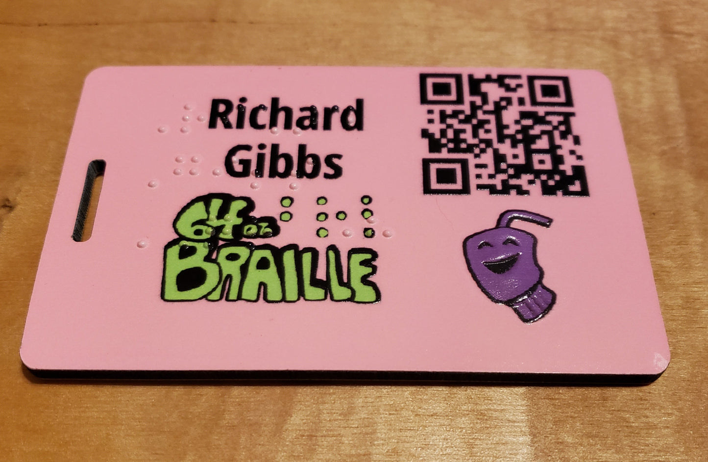 A luggage tag with a QR code for details,  braille for the person's name, and a textured version of our cup mascot