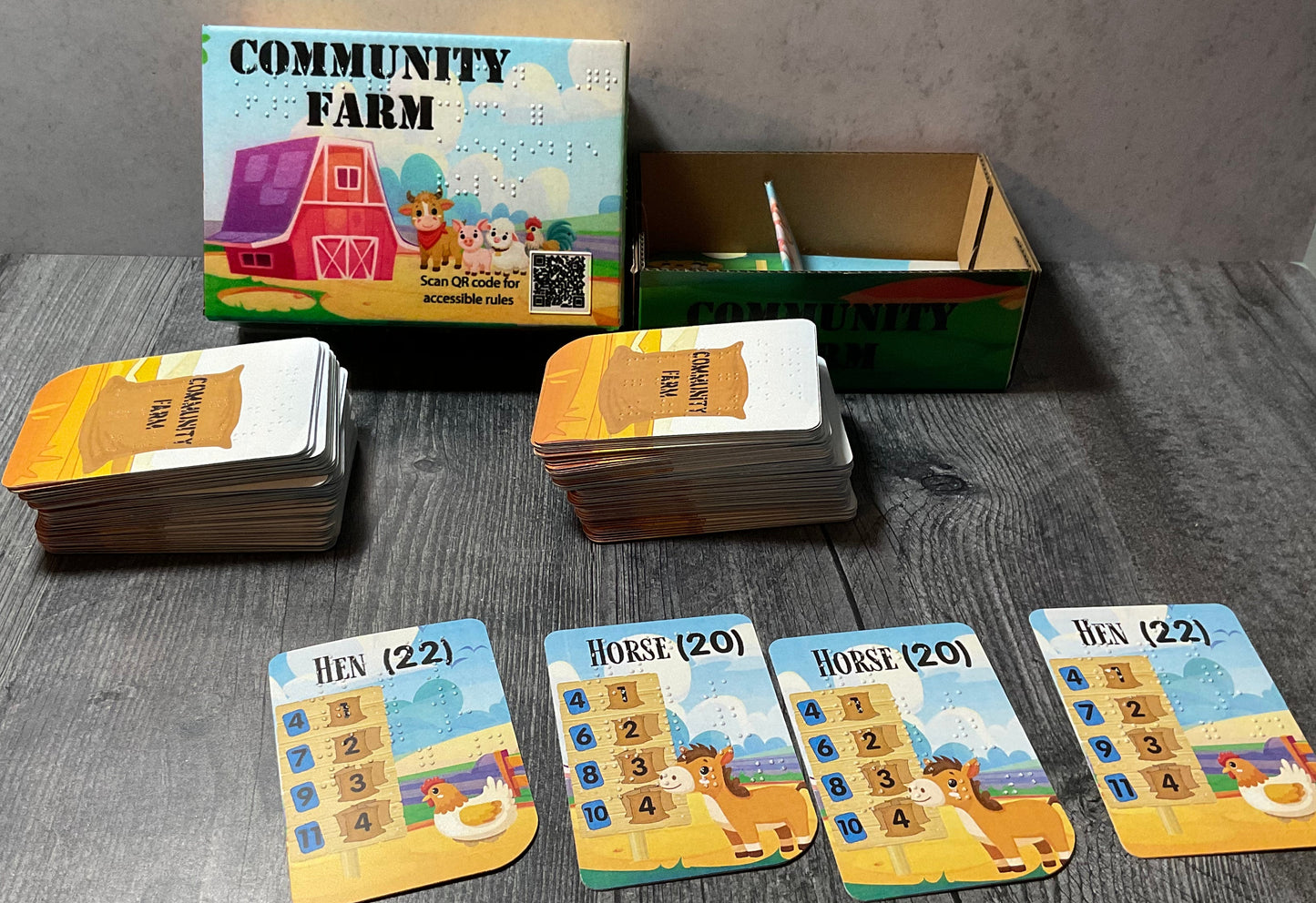 A shot of the community farm box with cards laid out in front of them. The cards have print and braille on them and show 2 hens and 2 horses.