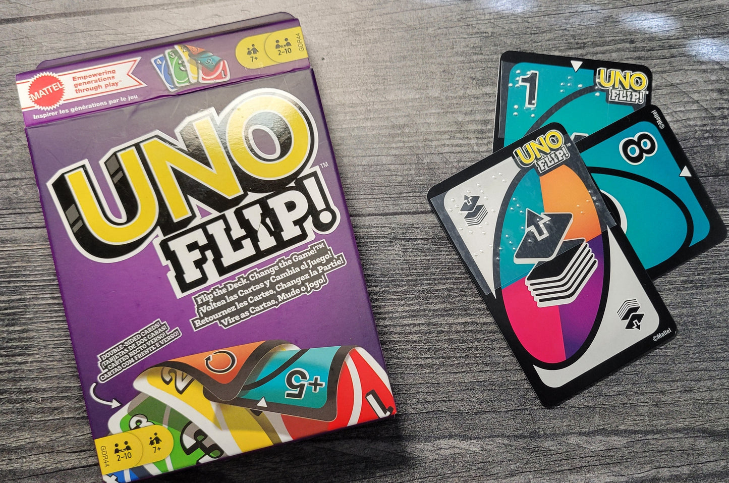 UNO Flip! game box and cards on a wooden surface. The cards have braille on them. The cards have braille on both sides but you can't see that.