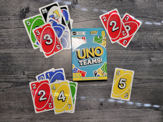 UNO Teams! card game box with selected cards on a wooden surface. All of the cards have braille stickers on them.