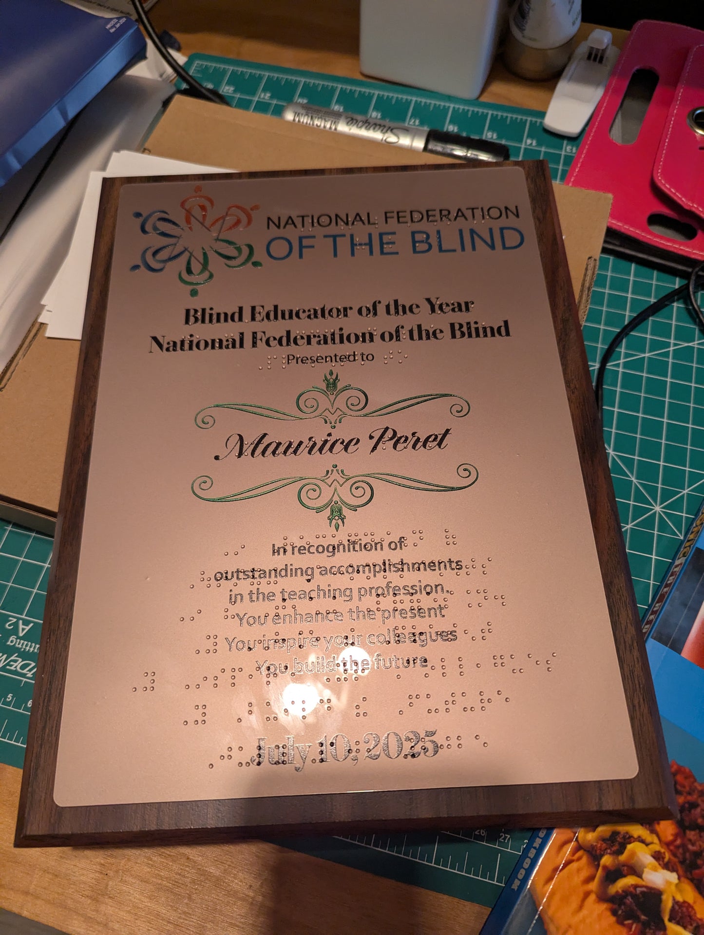 National Federation of the Blind award for Blind Educator of the Year on a table with office supplies. The award has print and braille on it and tactile shapes.

It is maple wood with an copper acrylic piece on it that the art is UV printed on.