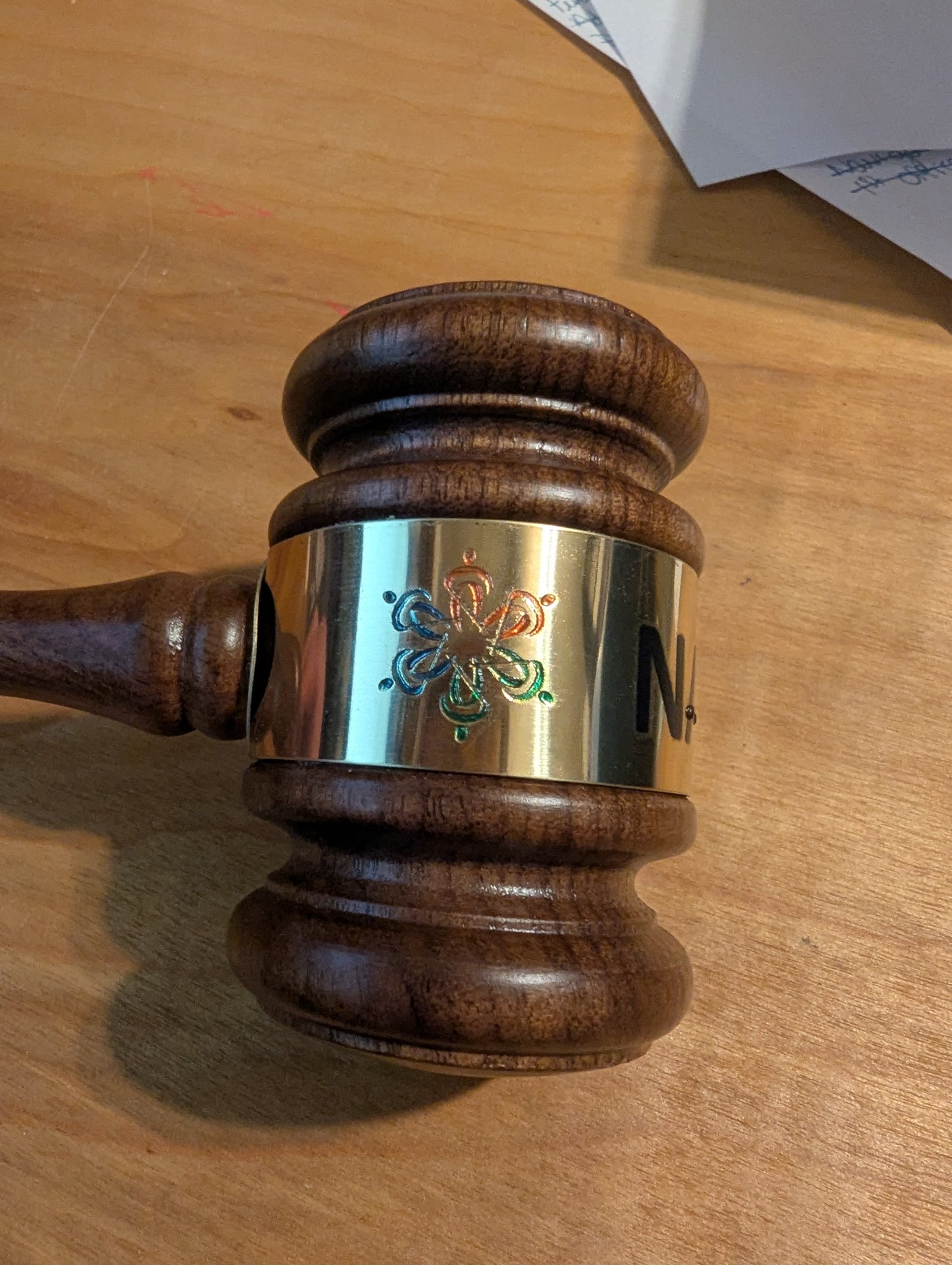 Wooden gavel with a metallic head on a wooden surface. The gavel has a tactile version of the NFB logo.