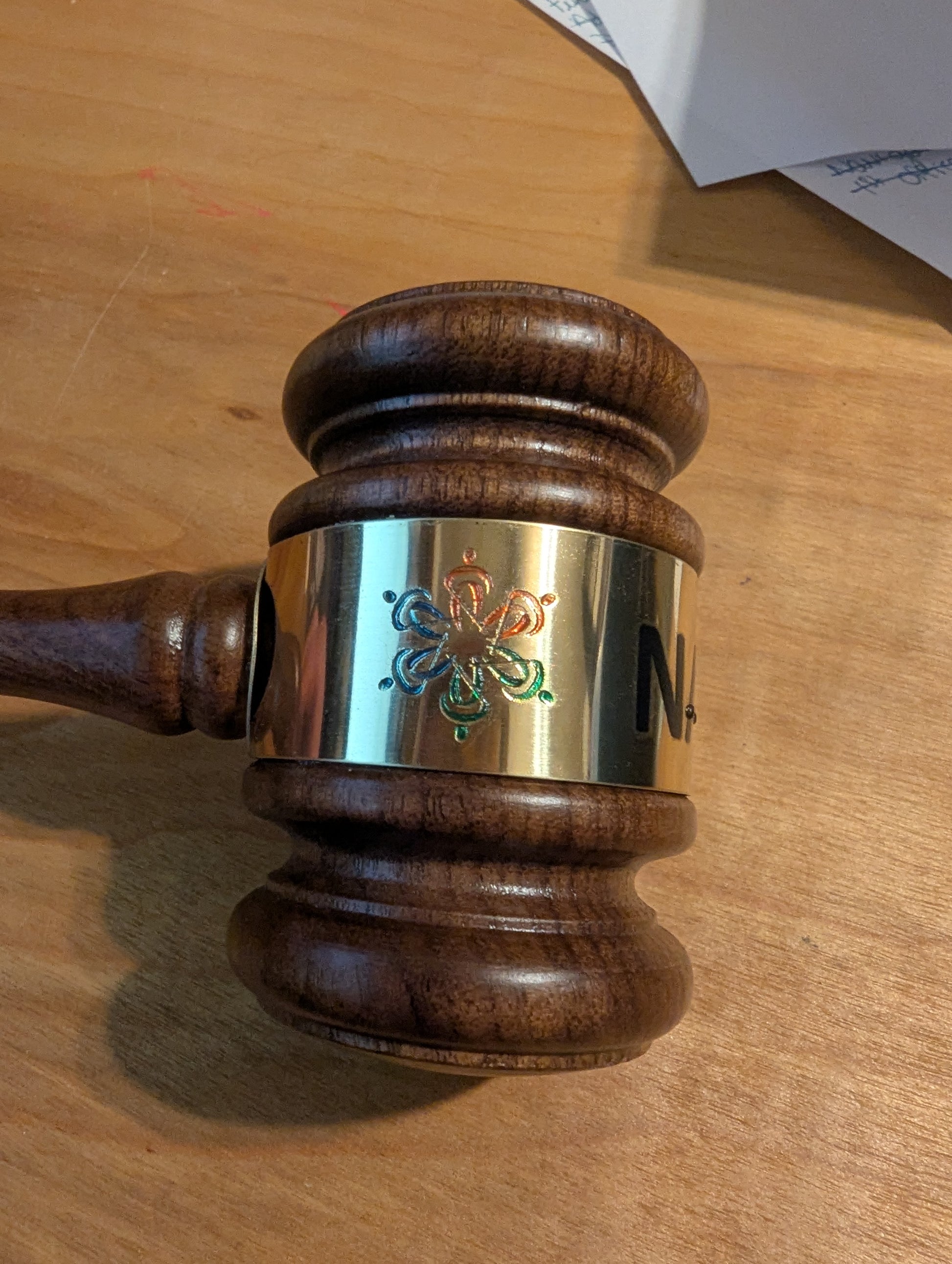 Wooden gavel with a metallic head on a wooden surface. The gavel has a tactile version of the NFB logo.