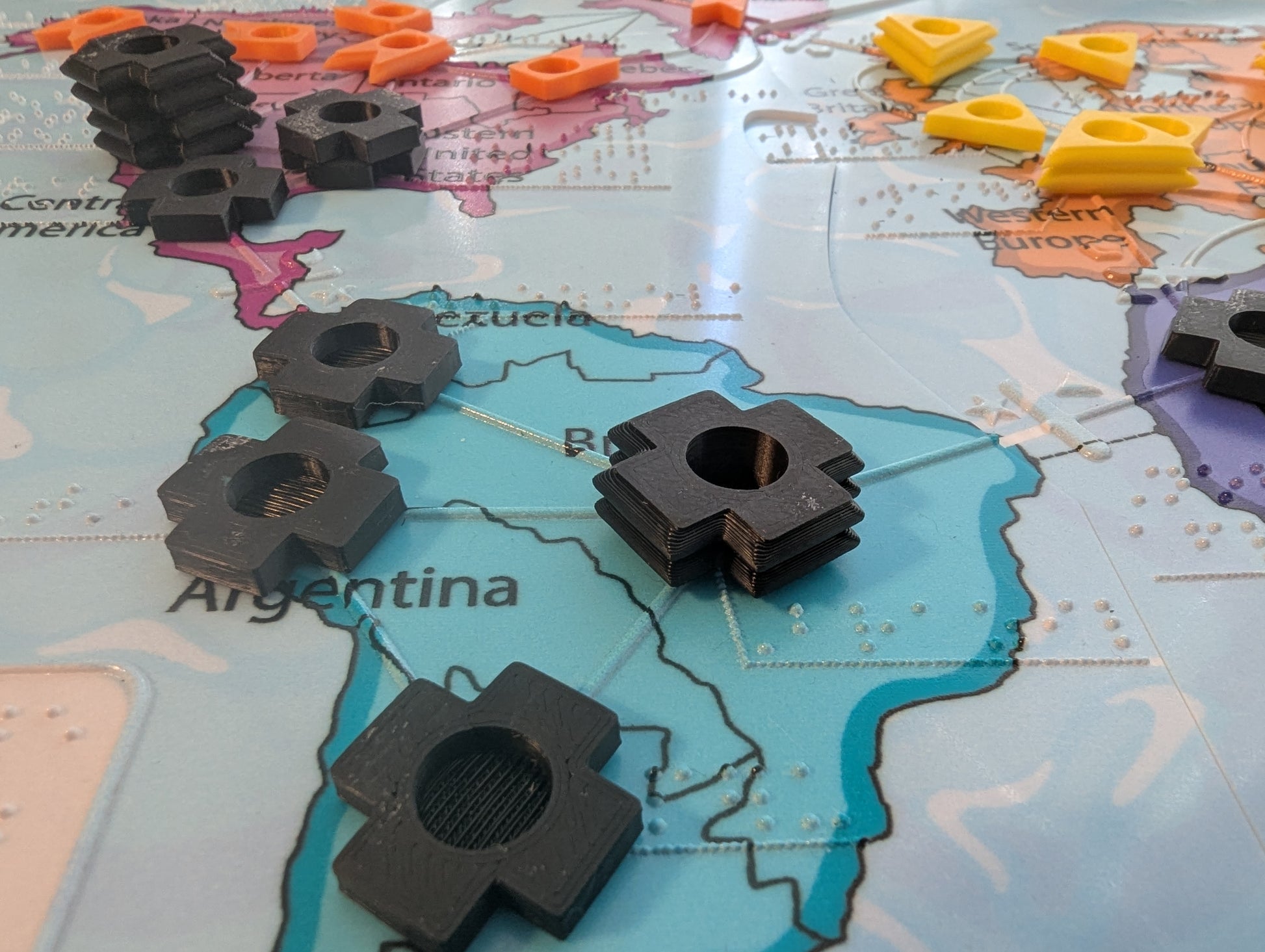 Black game pieces on a map of South America. The map has braille on it and tactile shapes denoting the border between South America and the other continents.