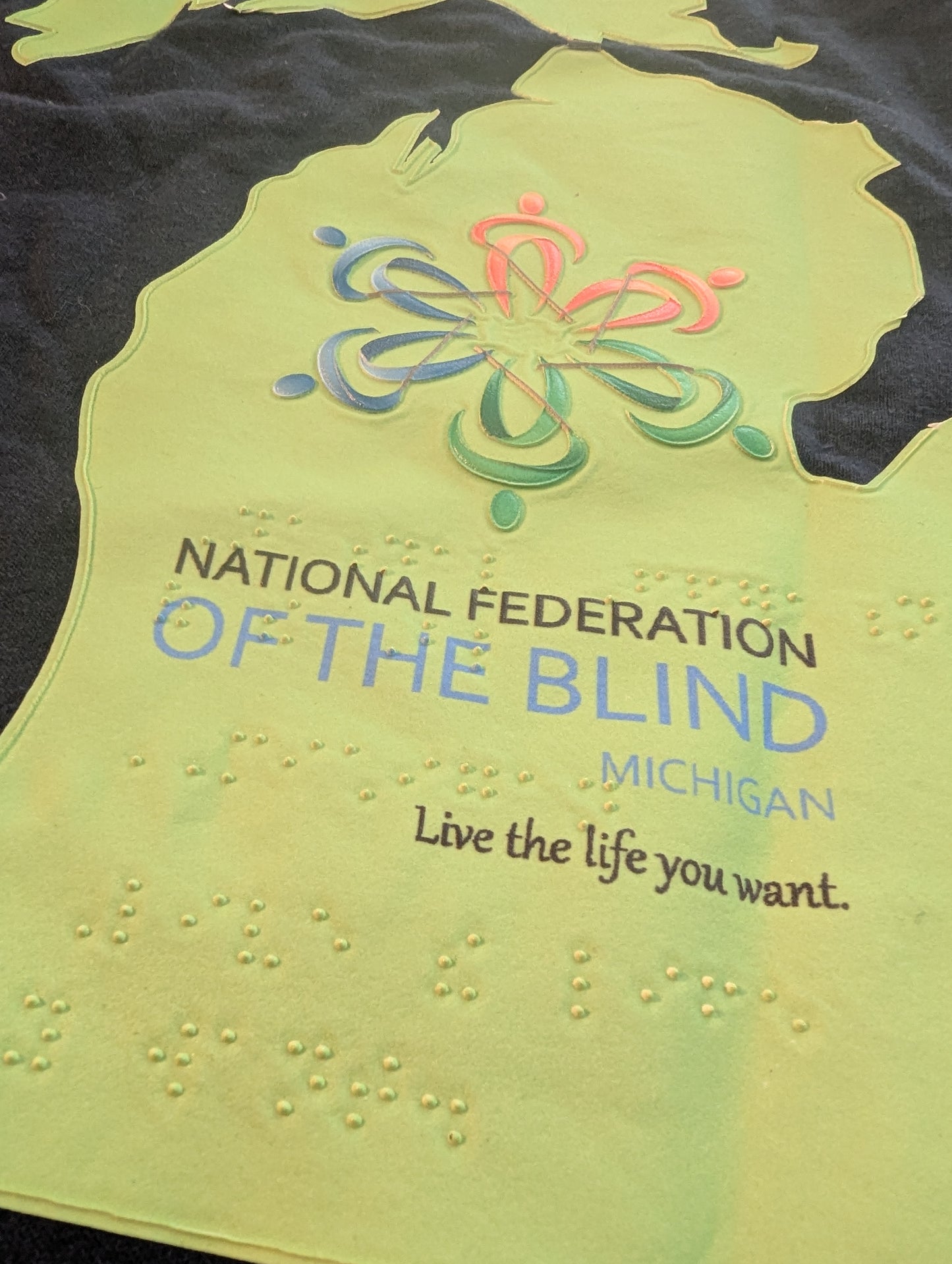 Green shirt with National Federation of the Blind Michigan logo and text. The shirt is tactile.