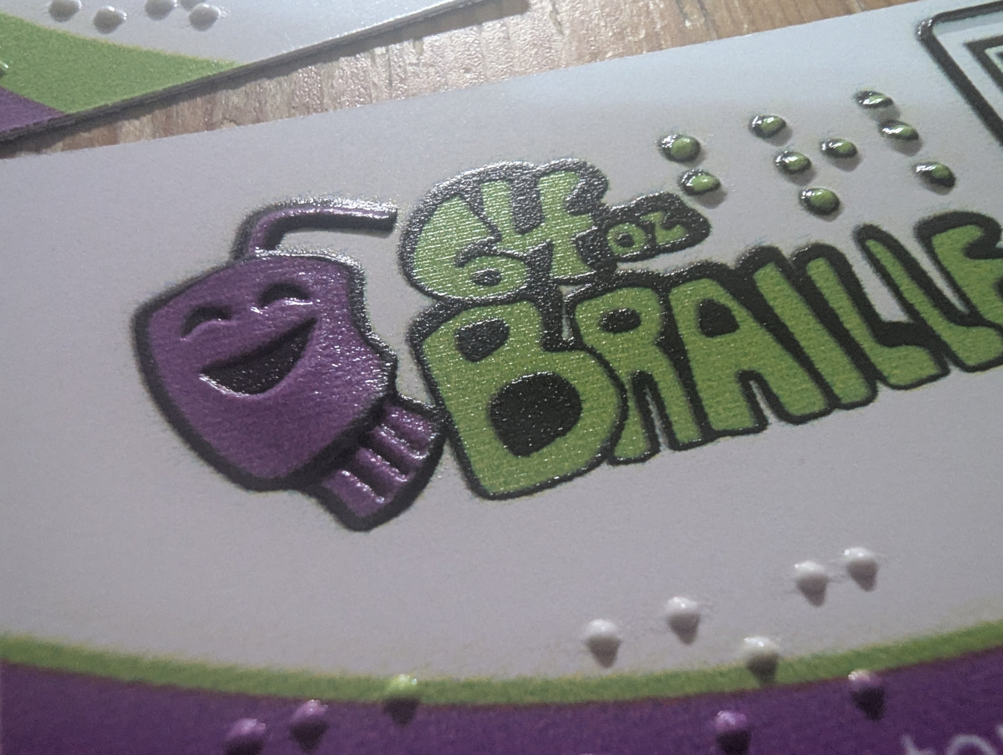 Logo with text '64 Oz. Braille' featuring a tactile purple cup logo on a white background.