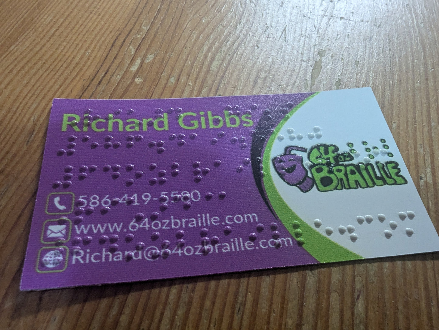 Business card with braille text and contact information on a wooden surface