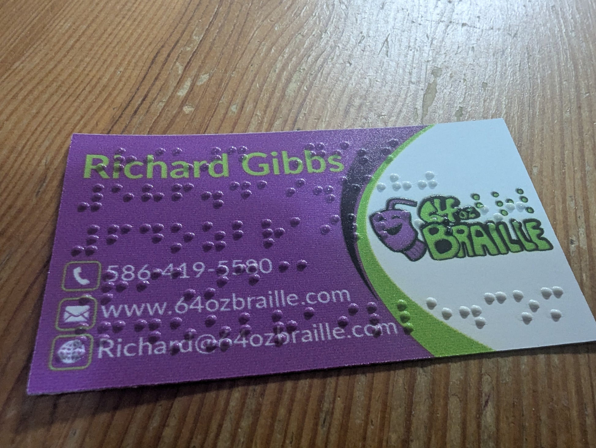 Business card with braille text and contact information on a wooden surface