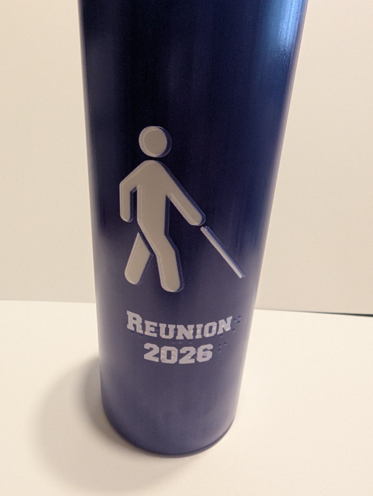 A dark blue insulated tumbler with a white walking figure icon and the text 'REUNION 2026' printed on the front, photographed against a plain light background.