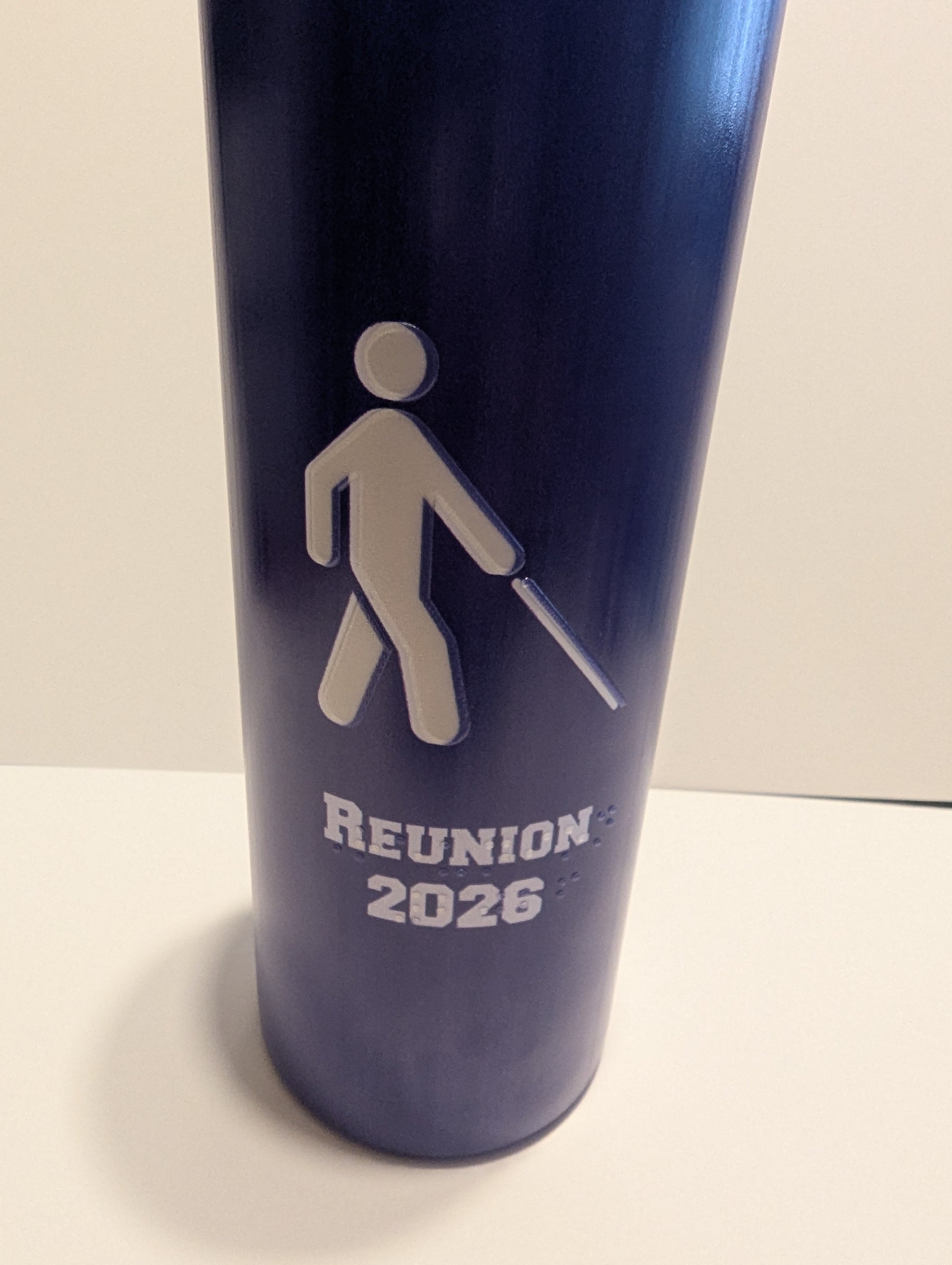 A dark blue insulated tumbler with a white walking figure icon and the text 'REUNION 2026' printed on the front, photographed against a plain light background.