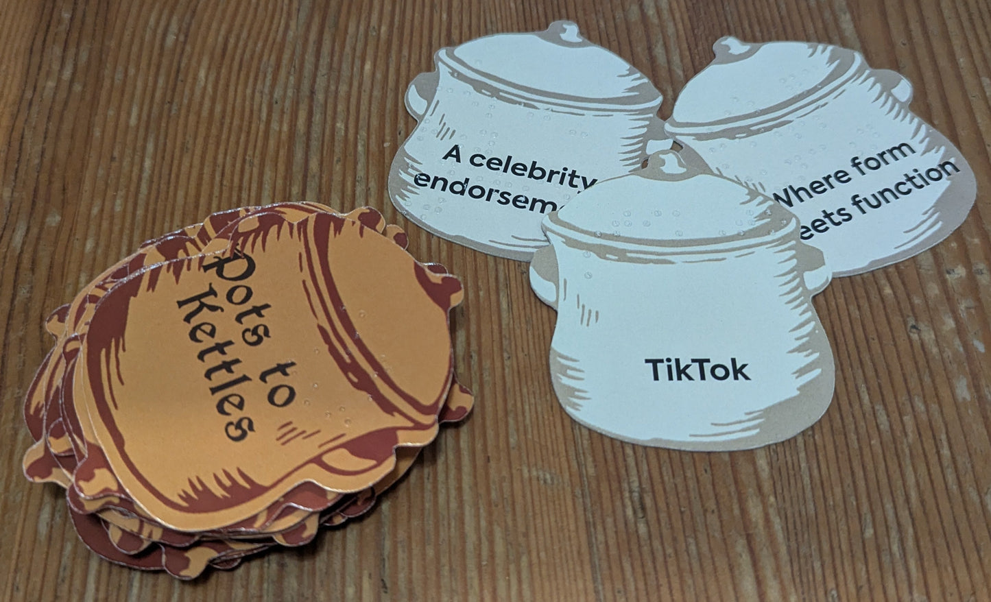 A close up on the pot cards. They are cut in the shape of pots and have words and concepts on them that might fit with the kettle card. The cards have both print and braille on them.
