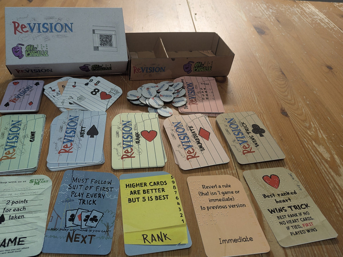 The box of Revision card, with the cards laid out in front and tokens displayed on a wooden tabletop. The custom playing cards, the rule change cards and round cardboard revision tokens.
All cards have both large print and Braille.
